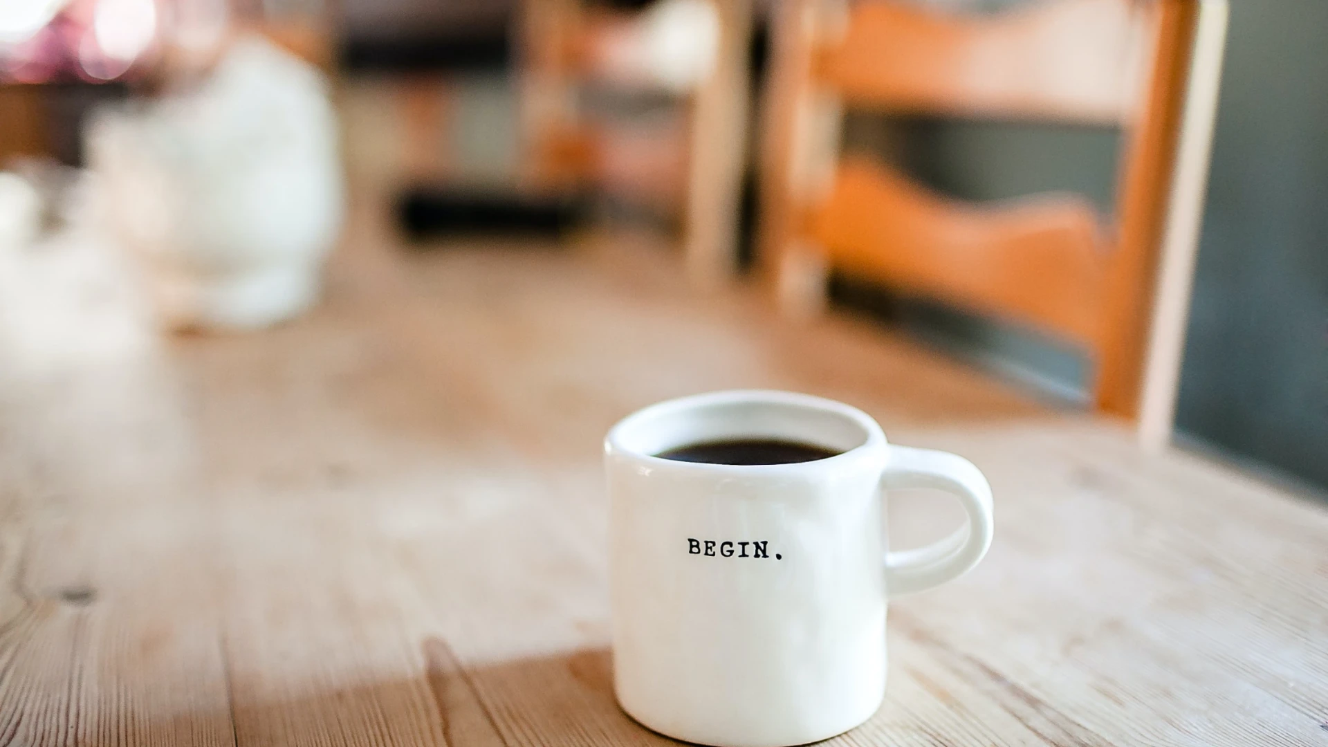 A white mug of coffee stamped with the word BEGIN on a café table